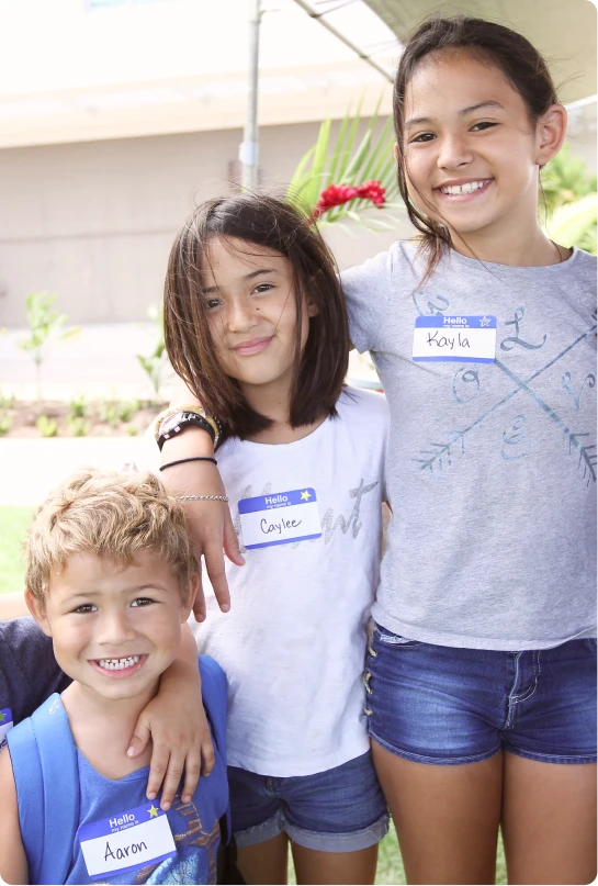 Three young kids of varying heights stand with arms around each other. 