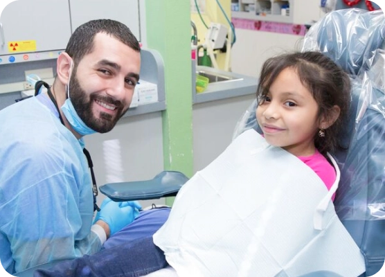 A dentist and his young patient smile at the camera during an exam.