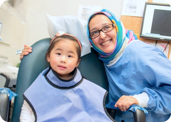 A young patient sits in an exam chair, a provider sits next to her smiling. 