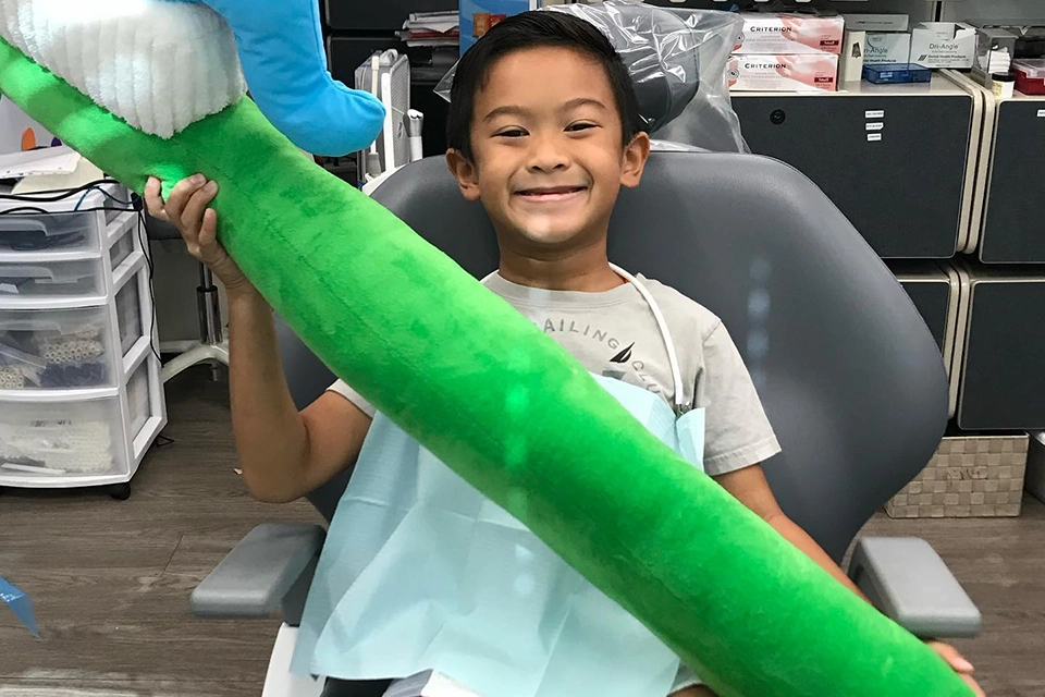 Young smiling boy in dentist chair holding a giant stuffed toothbrush