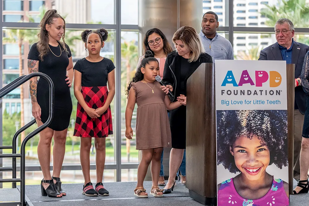 Several people at the AAPD foundation podium. A little girl speaking into a microphone.