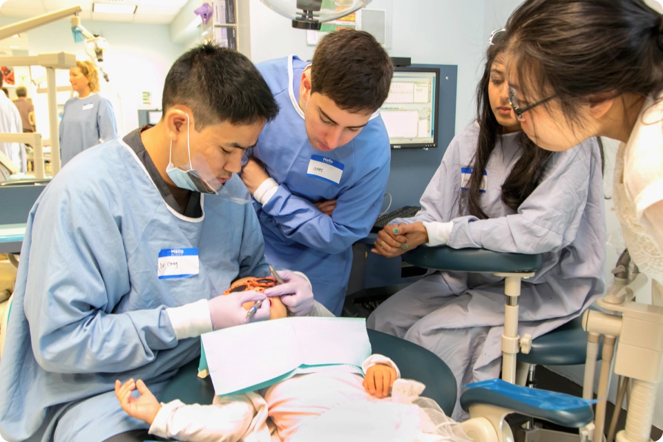 A dental professional working on a patient with 3 other professionals watching.